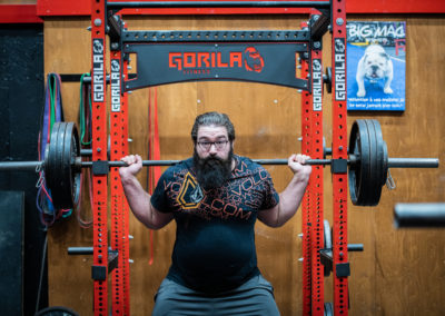 Homme barbu faisant des exercices de squat avec barre à poids lourd dans une salle de sport