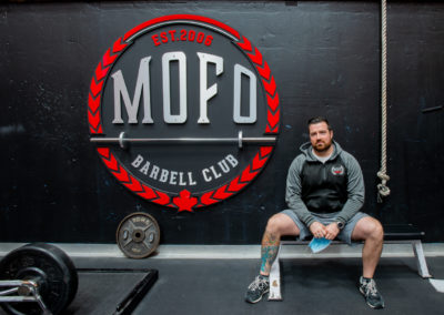 Homme assis devant un logo de club d'haltérophilie MOFO